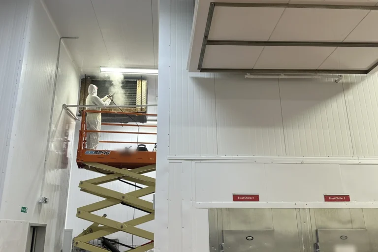 Engineer in a protective suit on a scissor lift cleaning a semi-industrial refrigeration evaporator at a food production site