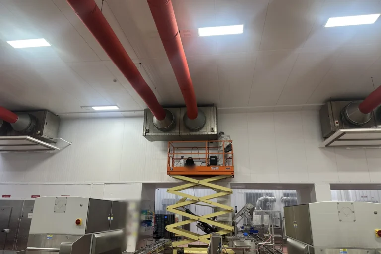 Large ceiling-mounted semi-industrial refrigeration evaporators being serviced from a scissor lift in a food production area